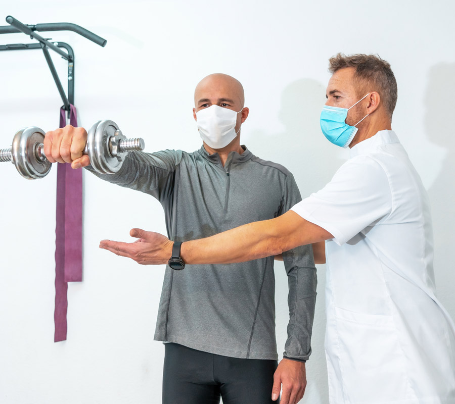 Physiotherapist with mask helping patient to exercise his back